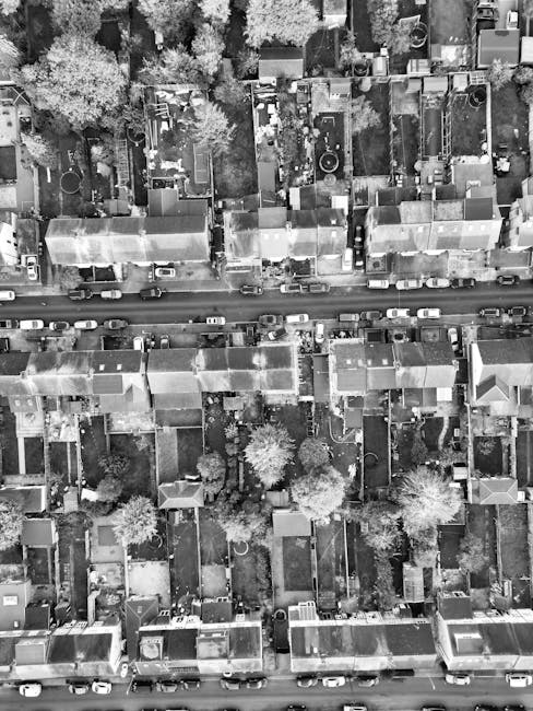 An aerial view of a densely populated residential area in Canning Town E16, showing a mix of small garden plots, lawns, and paved pathways. The gardens feature well-maintained grass lawns, some border
